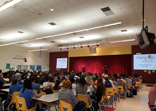 A group of teens sitting in a cafeteria listening to speakers